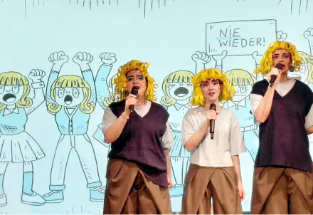 3 Menschen mit gelben Perücken im Comic-Stil, singend vor einer Grafik mit 6 Comicfiguren mit gelben Haaren. Eine der Figuren hält ein Schild mit "Nie wieder!" über den Kopf