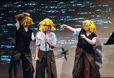 3 Menschen mit gelben Perücken im Comic-Stil und Mikrofonen in der Hand performen einen Song