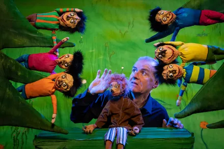 Puppenspieler mit sechs bunten Handpuppen mit schwarzen Haaren und großen Augen auf grünem Bühnenhintergrund