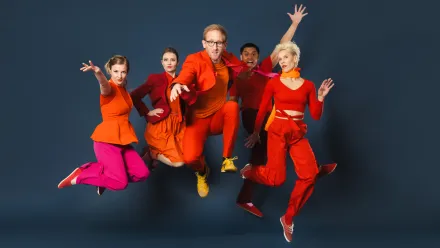 Fünf Personen in roter und pinker Kleidung springen vor dunklem, grau-blauen Hintergrund in die Luft