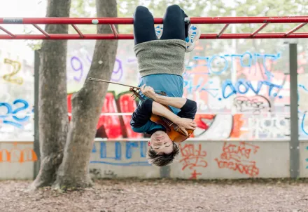 Ein Musiker hängt kopfüber an einer Stange und spielt Geige.