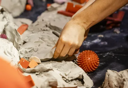 Nahaufnahme von Händen, die mit Ton und bunten Objekten arbeiten – ein kreativer Moment voller Struktur und Farbe.