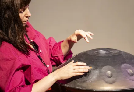Eine Musikerin in pinkem Hemd spielt konzentriert auf einer Handpan – ein Moment stiller Klangkunst.