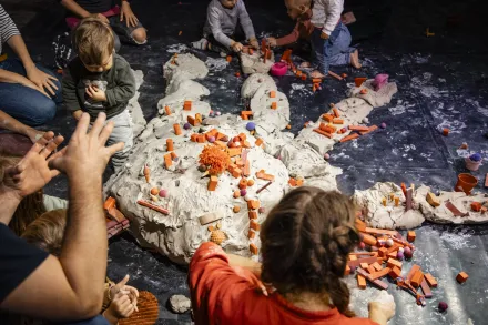 Kinder und Erwachsene formen mit Ton eine große Hand auf dem Boden und verzieren sie mit kleinen orangenen und violetten Tonstücken