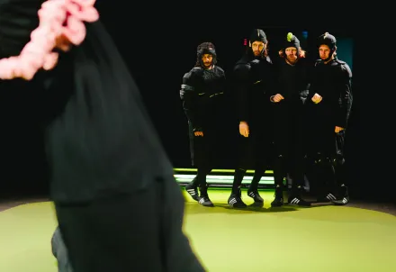 Vier Schauspieler in schwarzen Kostümen stehen dicht beieinander auf der Bühne.