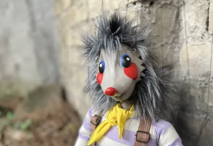 Eine bunte Puppe mit gestreifter Hose und gelbem Halstuch steht an einer Steinmauer.