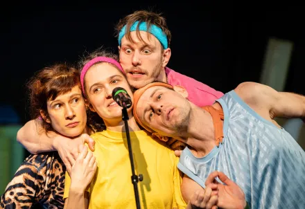 Vier Darsteller:innen drängen sich um ein Mikrofon und singen gemeinsam.