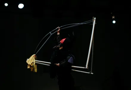 Performer*in in einem dunklen Bühnenmoment, eingerahmt von Licht und Bewegung.