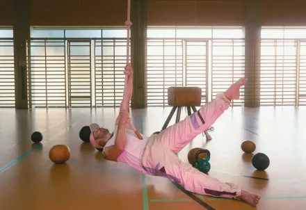 Performer*in in sportlicher Pose während einer Theaterszene in der Turnhalle.